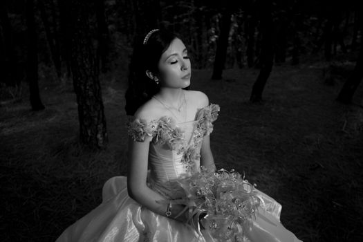 Black-and-white portrait of a young woman in a ball gown in a forest setting.