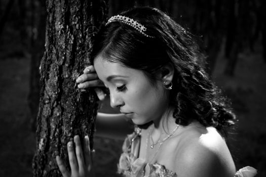 Elegant black and white portrait of a teenage girl wearing a tiara, leaning against tree bark outdoors.