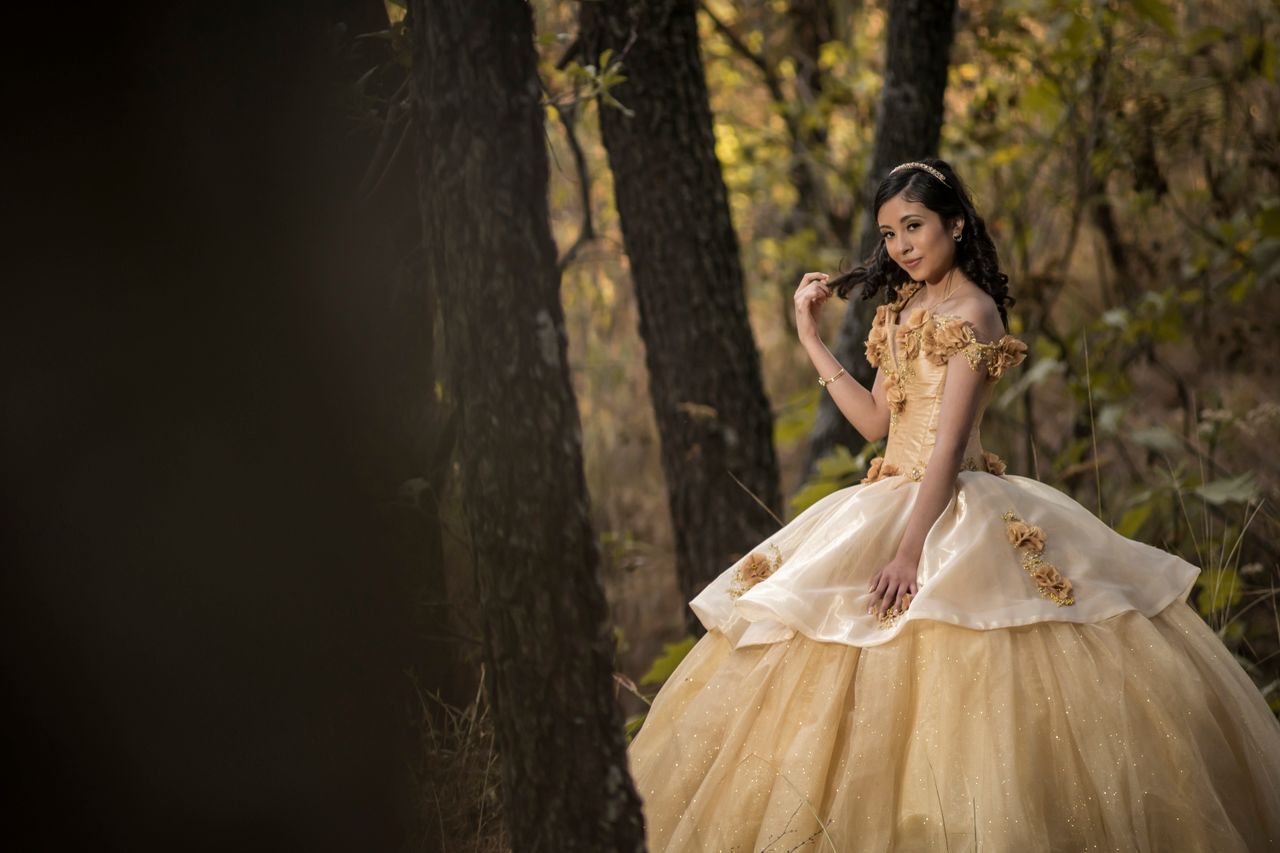 a teenager posing in an elegant ball gown amidst a serene forest setti
