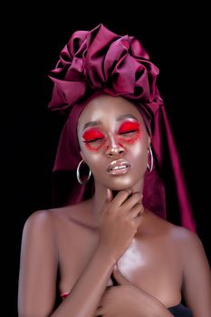 Artistic studio photo featuring a woman with vibrant makeup and headscarf against a black background.