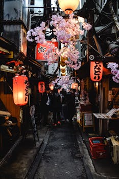 Explore a lively Japanese alley adorned with lanterns and cherry blossoms in an atmospheric street market.