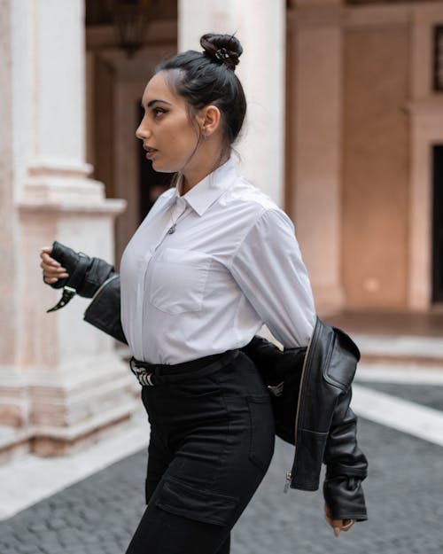 Stylish woman putting on leather jacket outside stone building