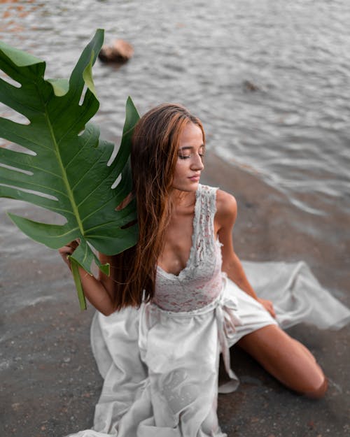 Graceful woman in chic dress sitting on wet beach