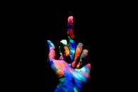 Crop anonymous persons hand painted with multicolored bright neon colors showing middle finger in obscurity