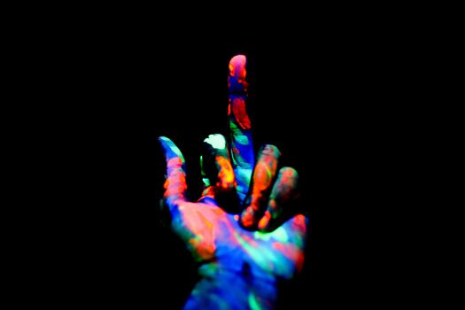 Crop anonymous persons hand painted with multicolored bright neon colors showing middle finger in obscurity