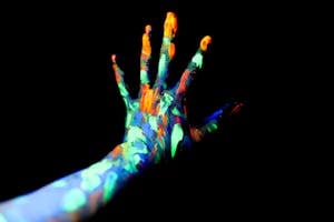 Crop unrecognizable persons hand with fingers spread covered with bright neon paints in dark studio