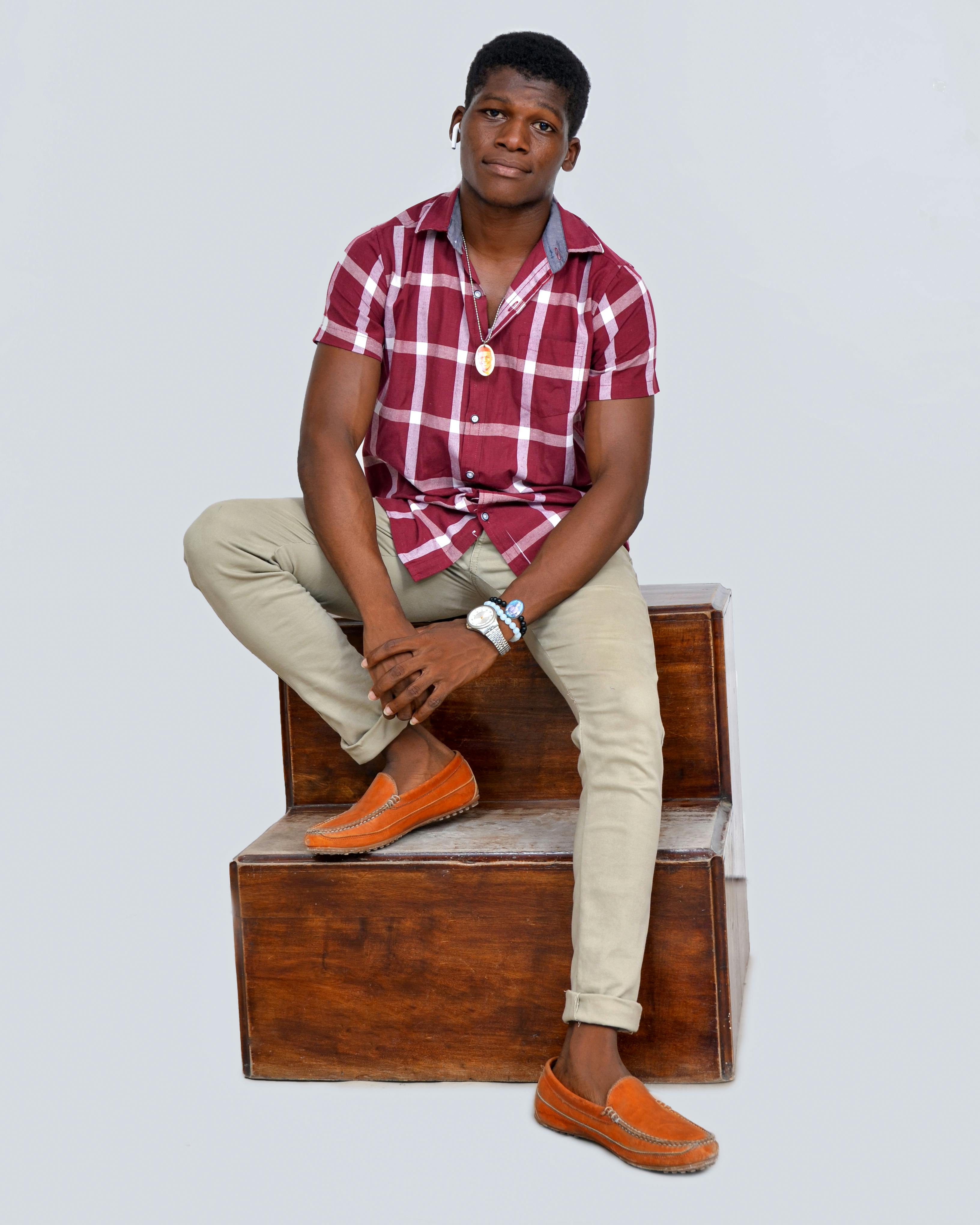 Smiling young man in checkered shirt and casual attire posing confidently.