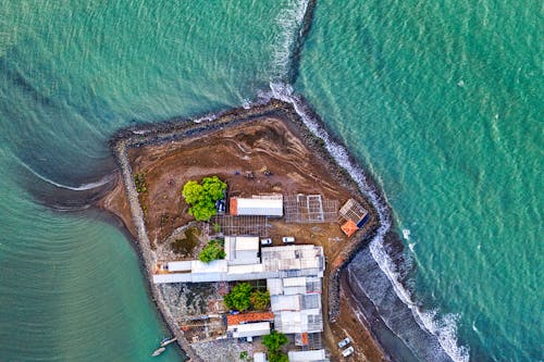 Picturesque drone view of rustic houses located on seashore washing by foamy waves on sunny day