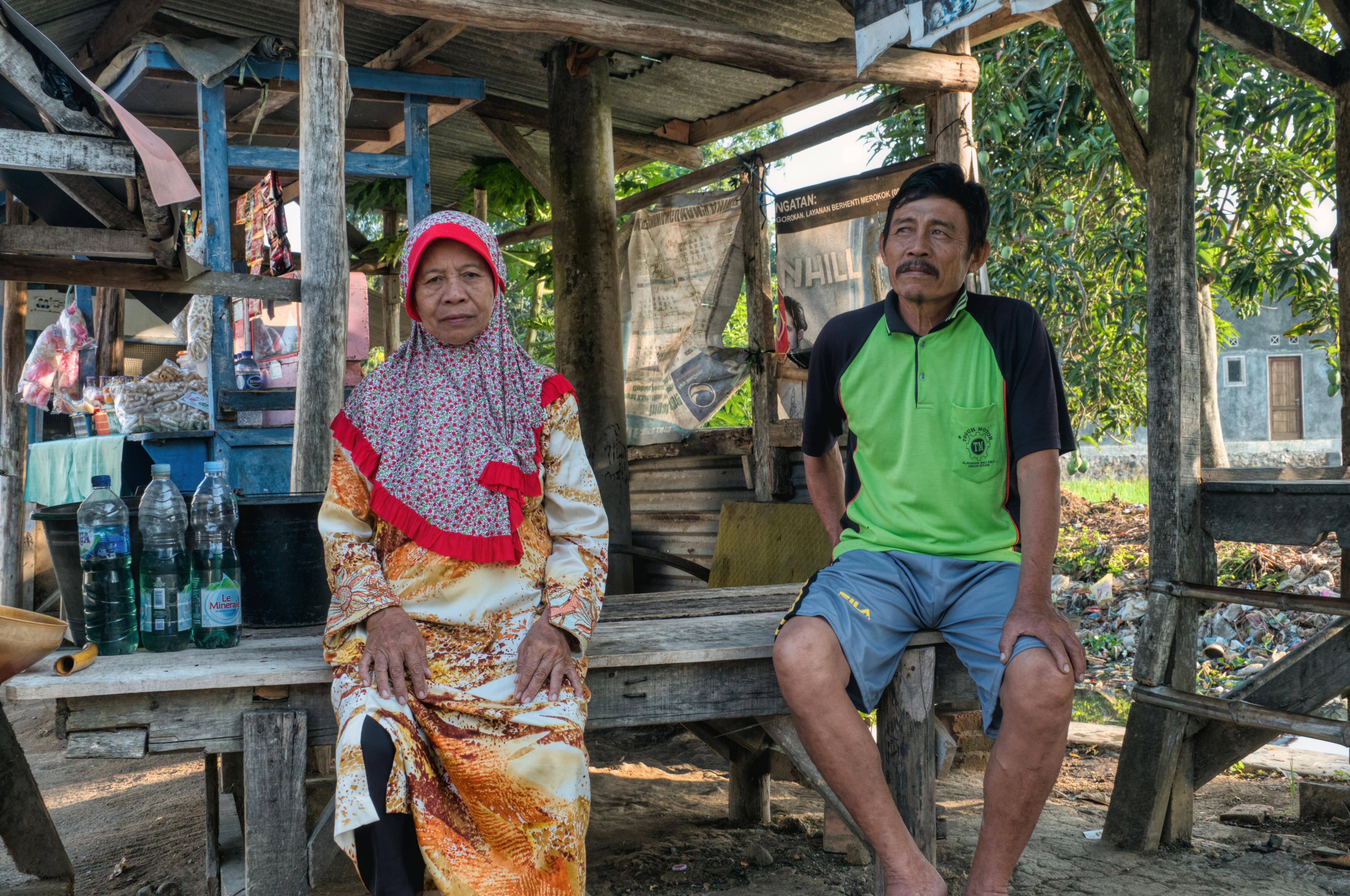 ethnic local man and woman siting in yard of village house in sunlight