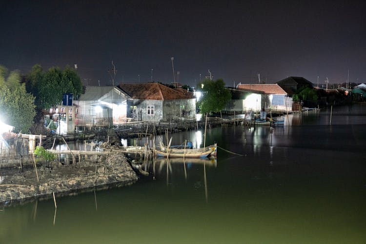 Boats Moored On Calm River In Village At Night