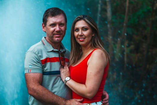 一对情侣在充满活力的户外环境中，微笑着在瀑布附近拥抱，展现了爱与团结