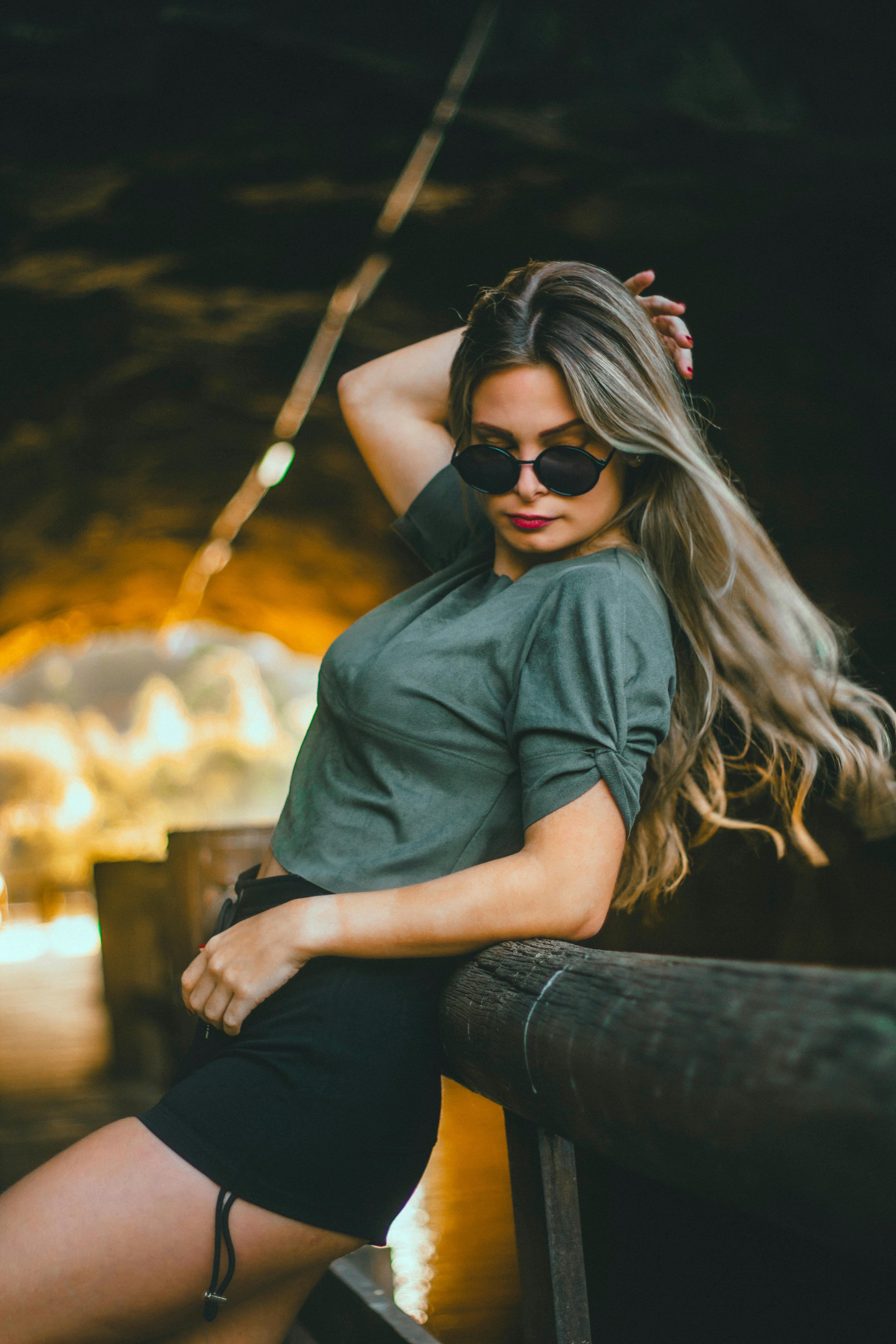 Free A fashionable woman wearing sunglasses strikes a pose outdoors in a vibrant setting. Stock Photo