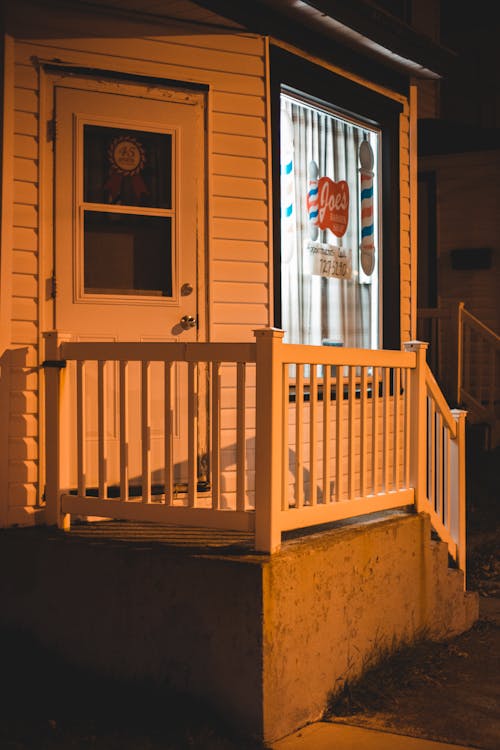 Exterior of wooden house with stairs with white railings and large windows in evening