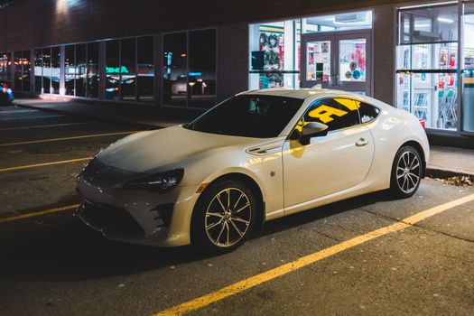 Expensive modern car parked on parking lot near entrance to supermarket at night