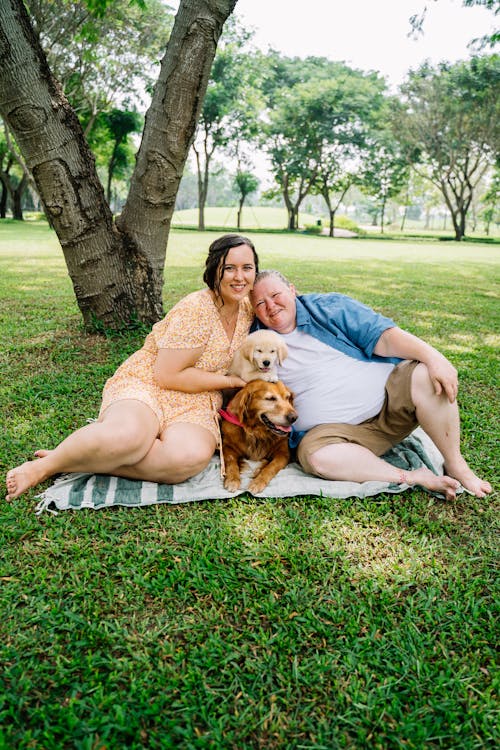 免費 男人和女人坐在棕色的狗旁邊的草地上 圖庫相片