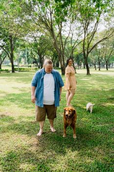两个成年人和一只金毛猎犬、一只小狗在阳光明媚的公园里享受美好的一天