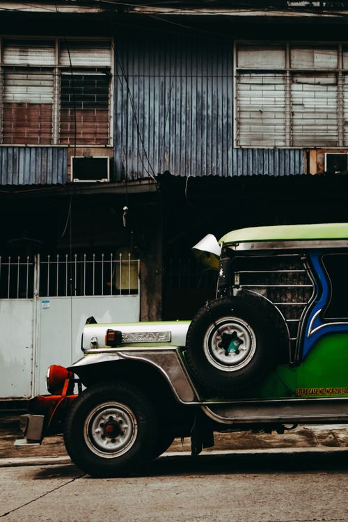 Free A vibrant jeepney parked in front of an urban building, showcasing street photography. Stock Photo