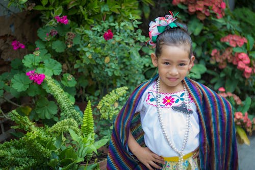 Photo of a Kid in Traditional Clothes Posing Near Plants