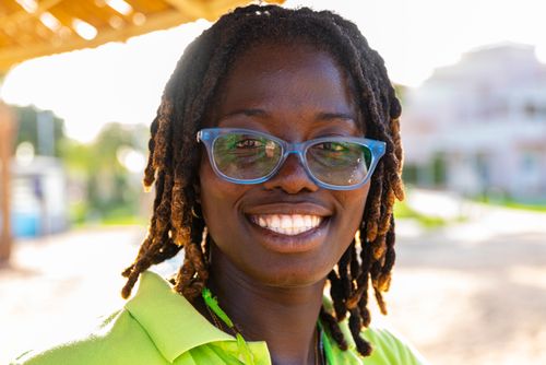 Free Portrait of a cheerful woman wearing blue eyeglasses with a sunny outdoor background. Stock Photo