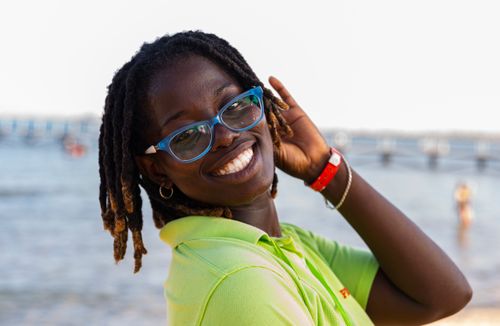 Free Joyful young woman in glasses and green shirt smiling on a sunny day at the beach. Stock Photo
