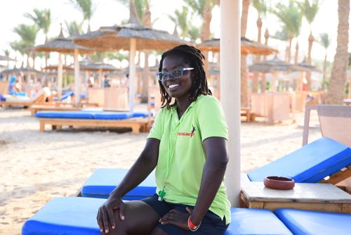 Free Lifeguard smiling on a tropical beach, sitting on a sunbed under straw umbrellas. Stock Photo