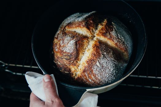 From above of crop anonymous chef pulling out fresh crispy bread from oven