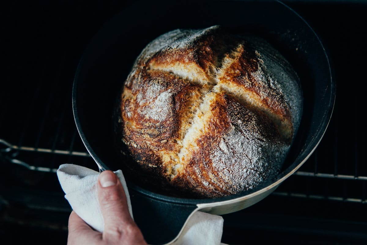 From above of crop anonymous chef pulling out fresh crispy bread from oven
