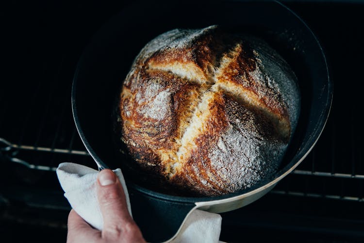 Person Pulling Out Freshly Baked Bread From Oven