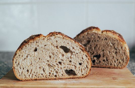 Cut slices of wheat bread loaf placed on wooden cutting board at kitchen