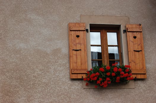 迷人的窗户装有心形镂空木百叶窗，乡村墙壁上挂着充满活力的红花