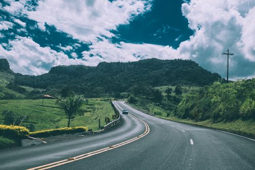 Free A picturesque road winding through the countryside with mountains in the background under a blue sky. Stock Photo