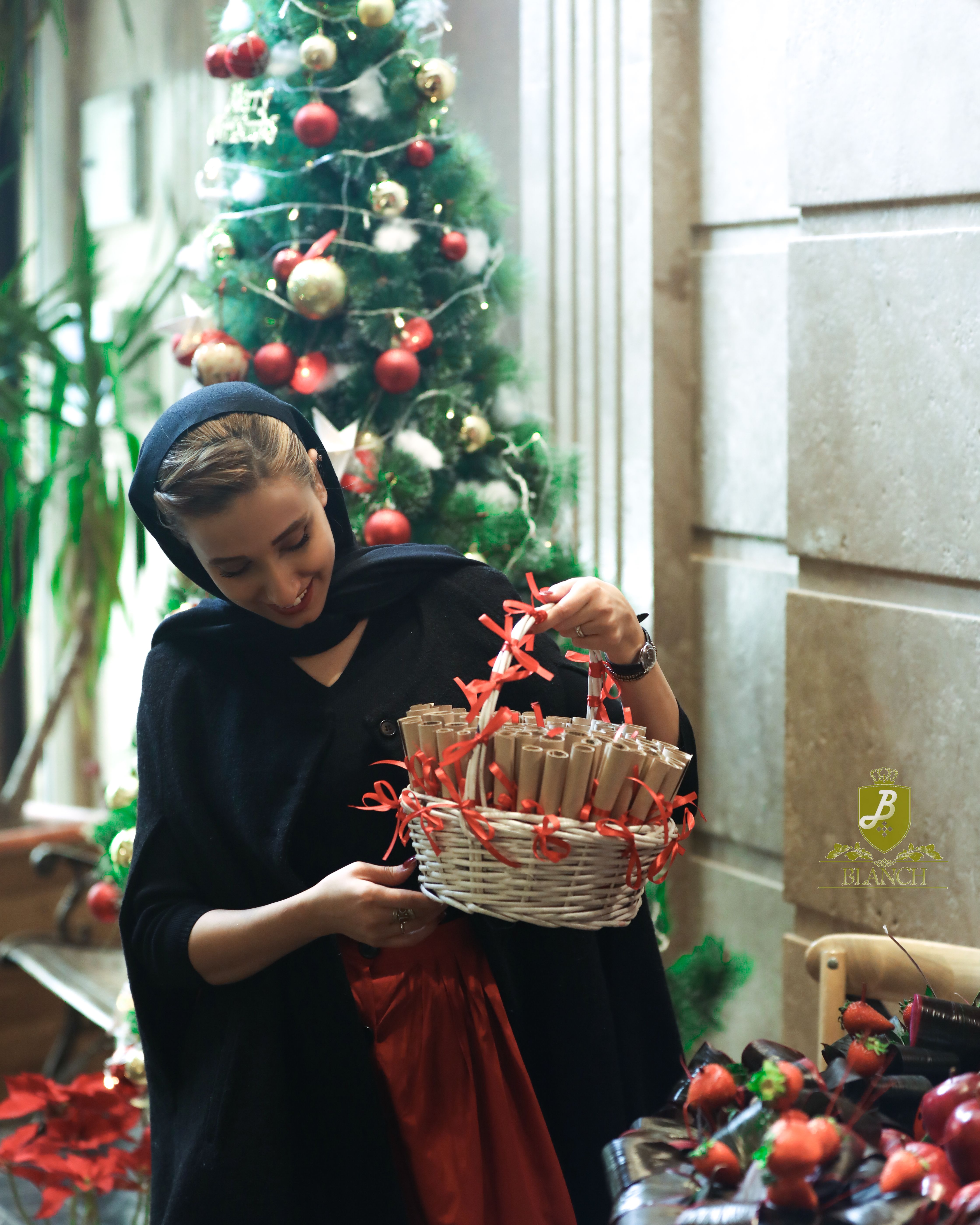 Woman in hijab holding a basket next to a decorated Christmas tree indoors.