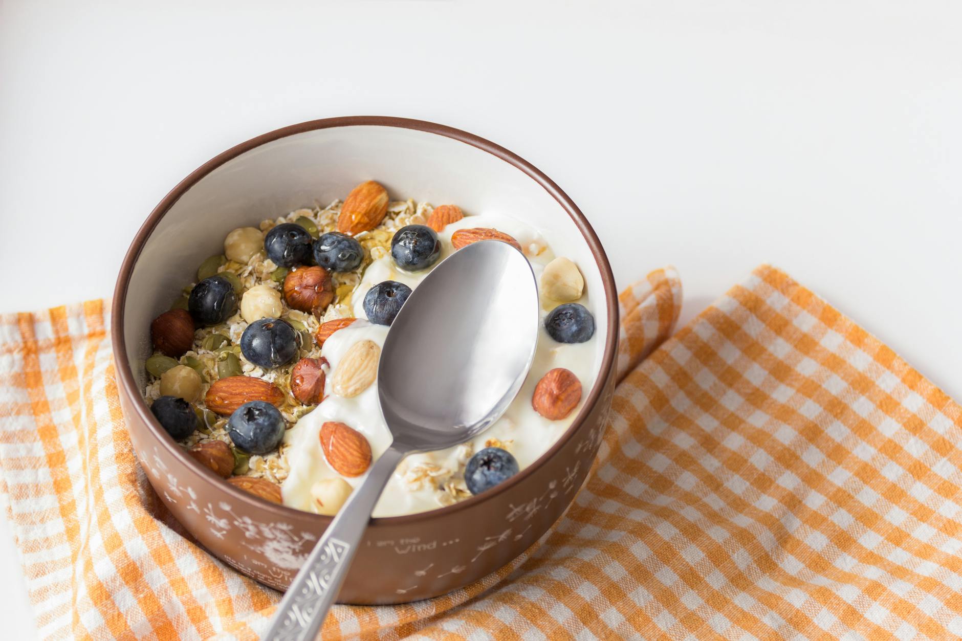 A delicious breakfast bowl featuring yogurt, nuts, and fresh blueberries on a checkered cloth.