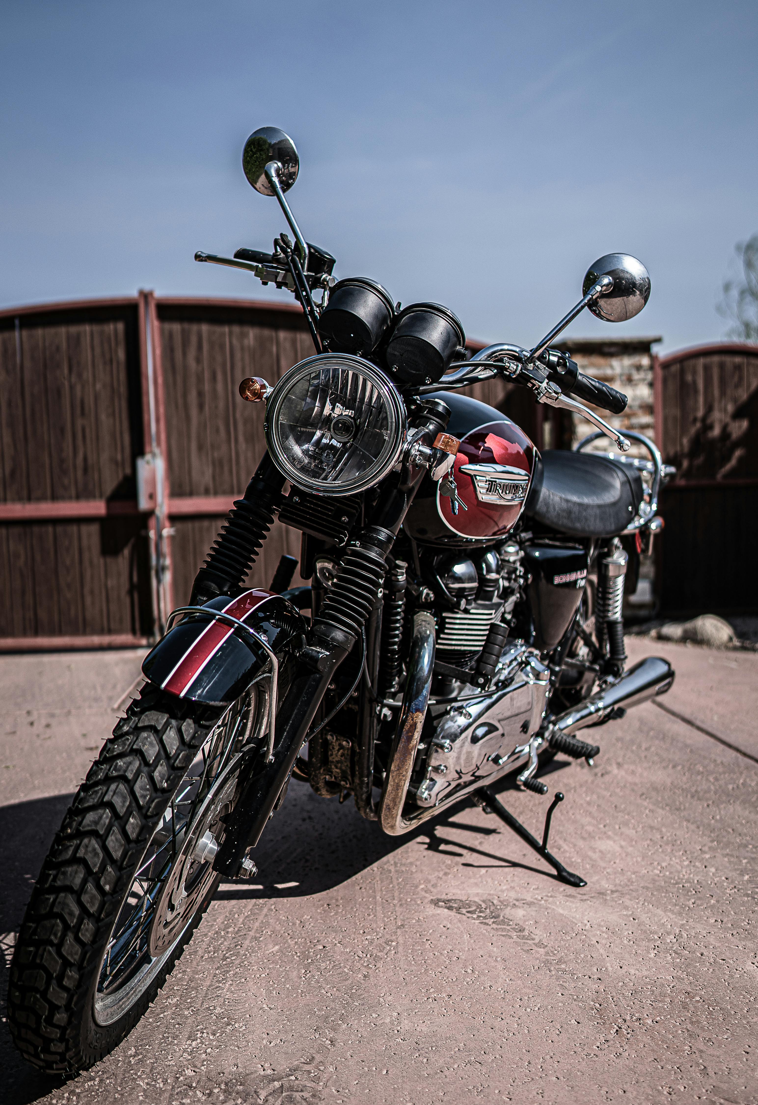 Black and red retro motorcycle with chrome details parked on asphalt road against cloudless blue sky