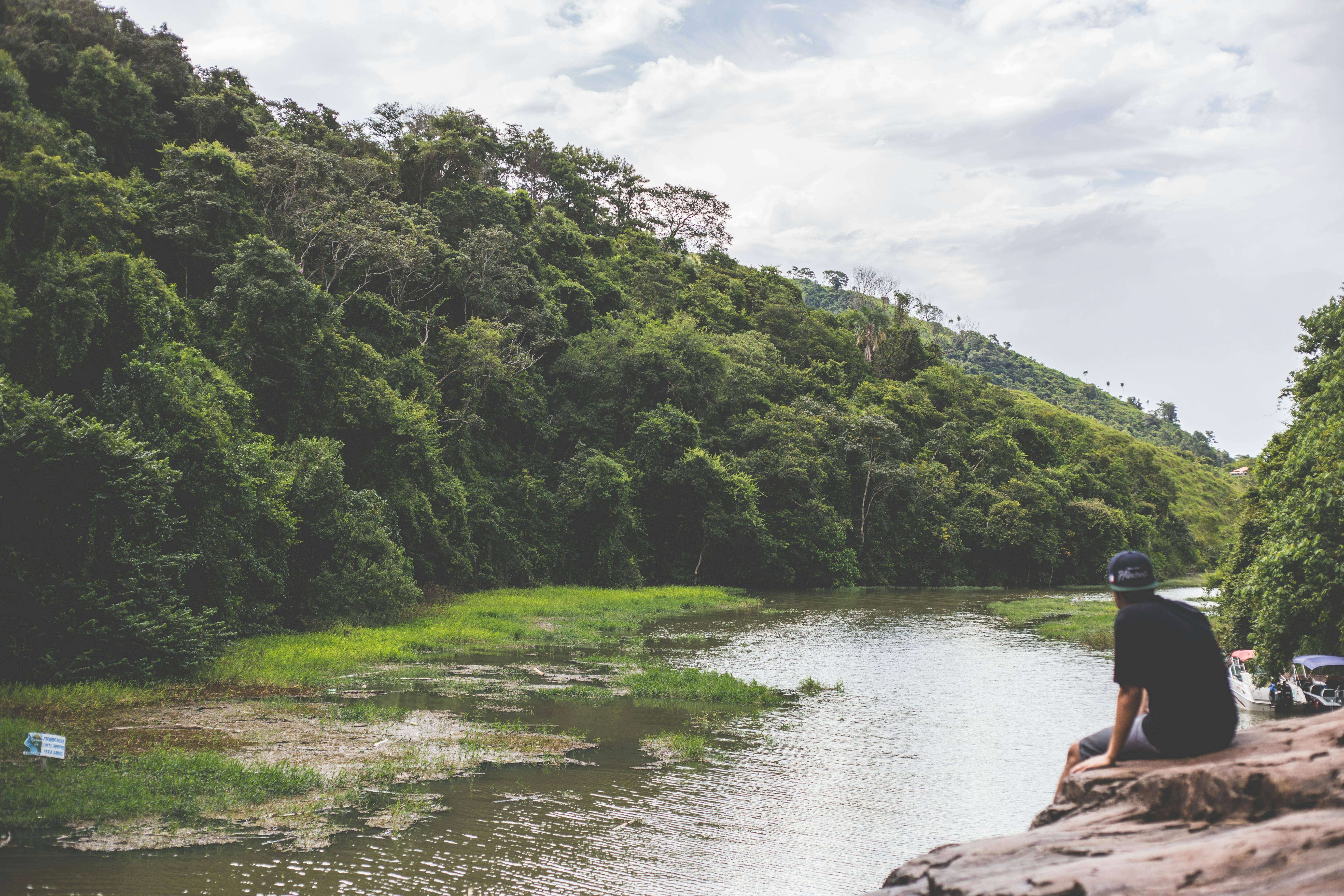 在宁静的河流旁，一个人放松身心，周围环绕着充满活力的绿色森林和岩石地形