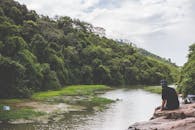 在宁静的河流旁，一个人放松身心，周围环绕着充满活力的绿色森林和岩石地形