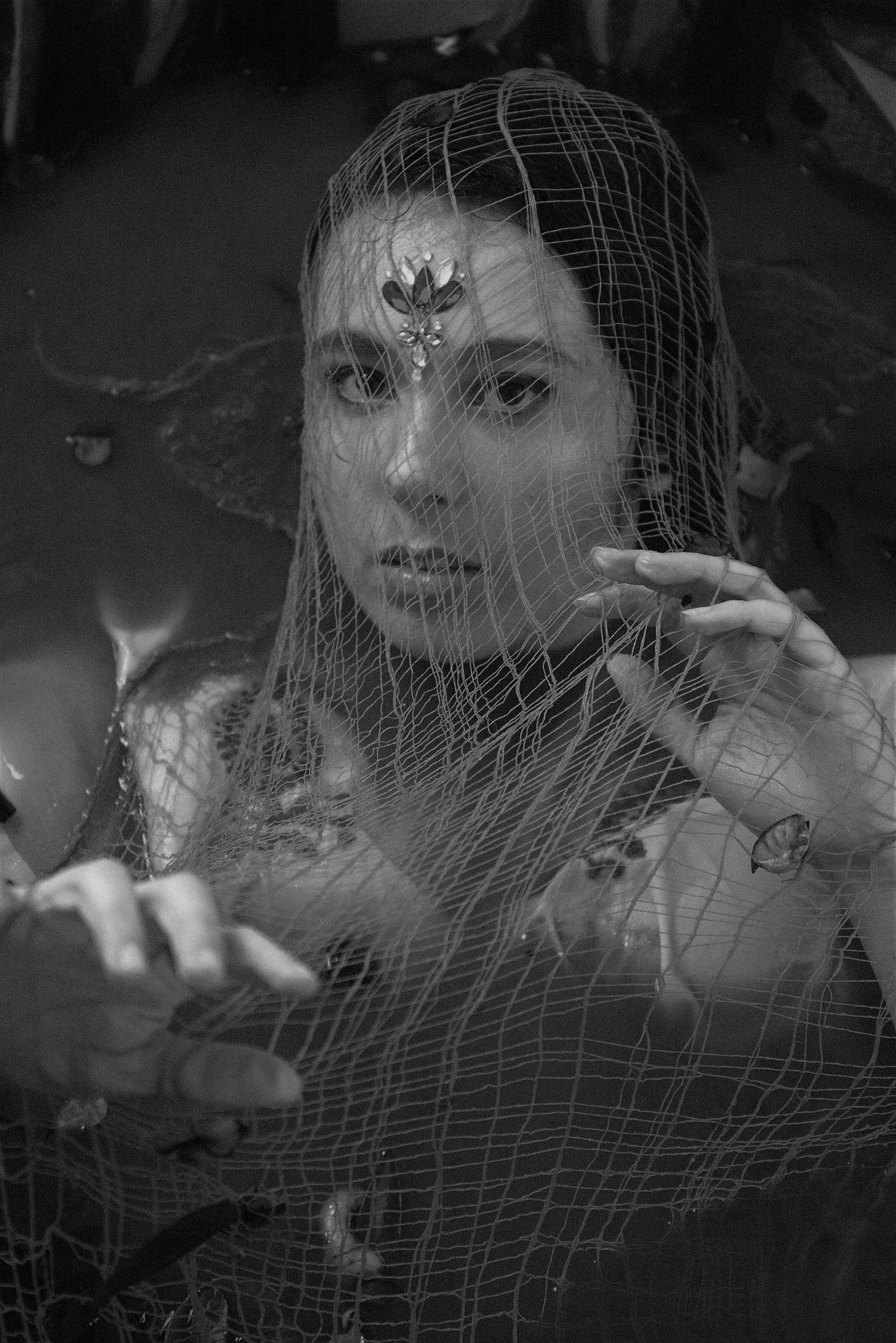 Artistic black and white portrait of a woman enveloped in netting, evoking mystery and introspection.