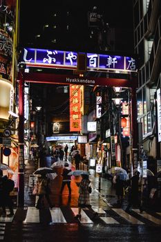 日本涉谷繁忙的街景中，人们打着伞在夜间行走