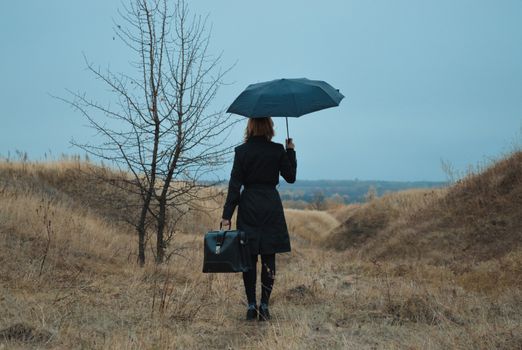 一个女子撑着伞，独自站在秋日阴沉的田野里