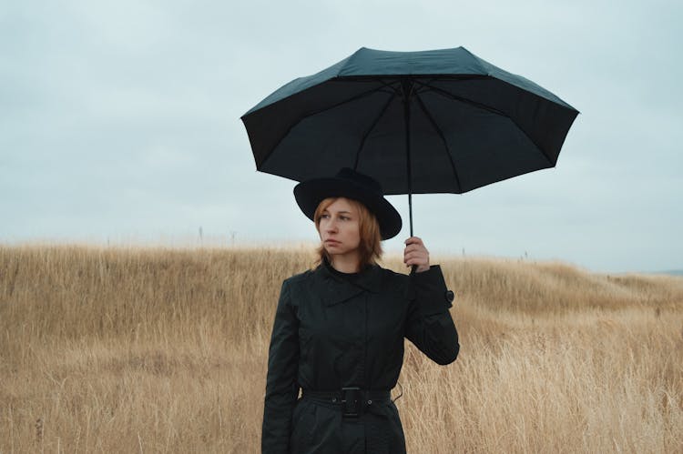 Sad Woman With Umbrella Standing In Field And Looking Away