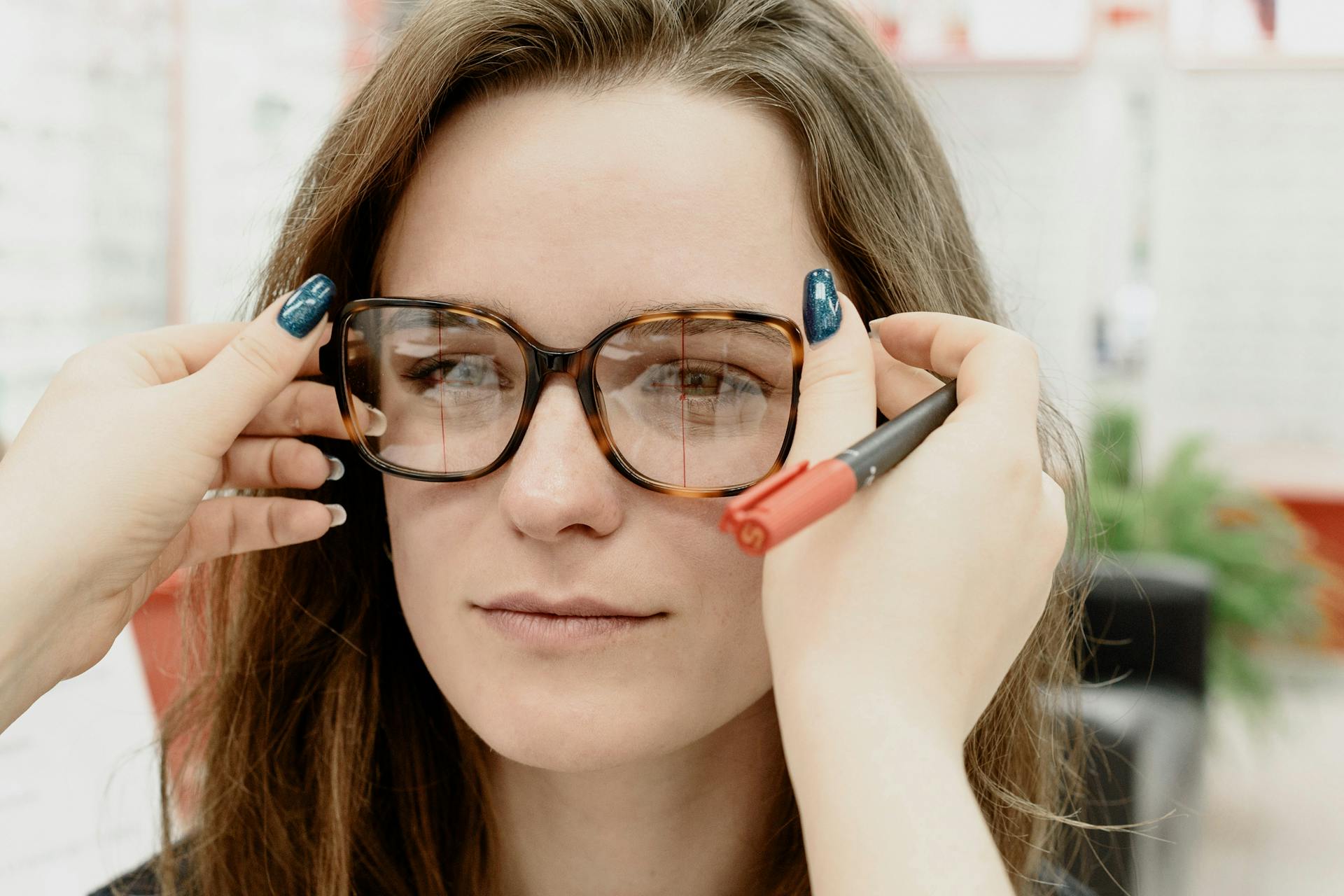 Close-up of a female patient getting glasses adjusted by an optician inside a clinic.