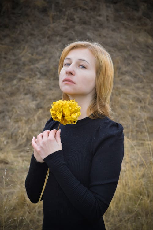 Sad young woman with flower standing in nature and looking at camera