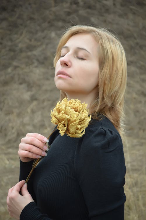 Upset young woman with flower relaxing in autumn nature with closed eyes