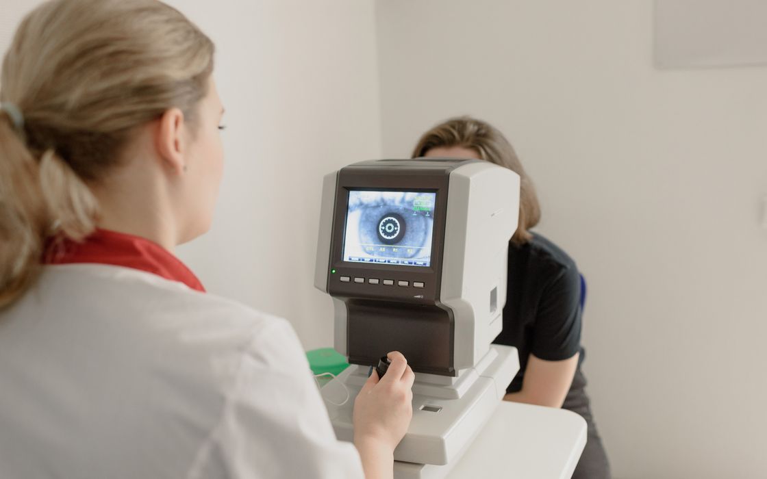 Eye specialist operating a computerised eye-measurement device while a patient looks into it, with an image of the eye on the screen