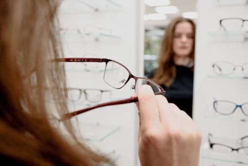 Back view of female client standing with rim while choosing eyeglasses in ophthalmology shop