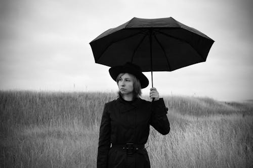 Elegant pensive female standing in meadow with umbrella and looking away