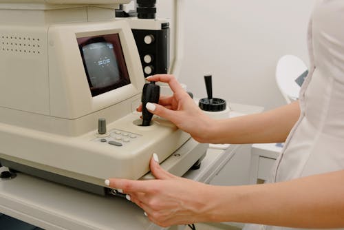 Free Side view of crop faceless female ophthalmologist using autorefraktometer for corneal topography in contemporary medical office Stock Photo