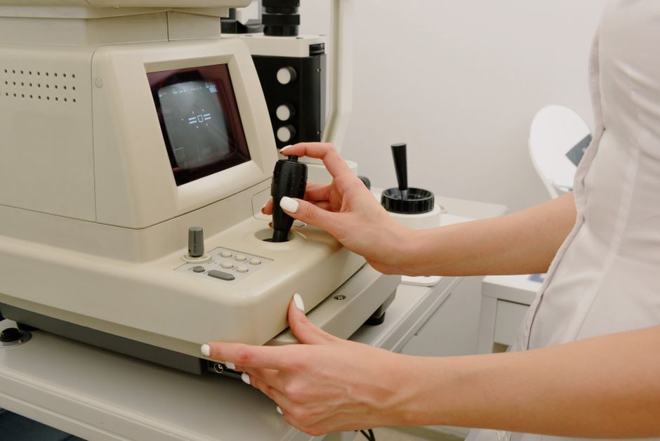 optometrist recommended eye care products - Side view of crop faceless female ophthalmologist using autorefraktometer for corneal topography in contemporary medical office