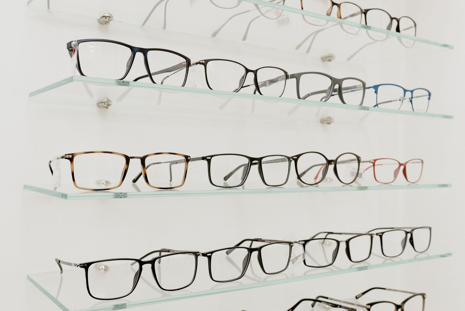 A variety of eyeglasses displayed on clear glass shelves in a retail store.