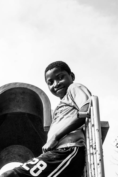 Grayscale Photo of Smiling Boy Leaning on Metal Railing